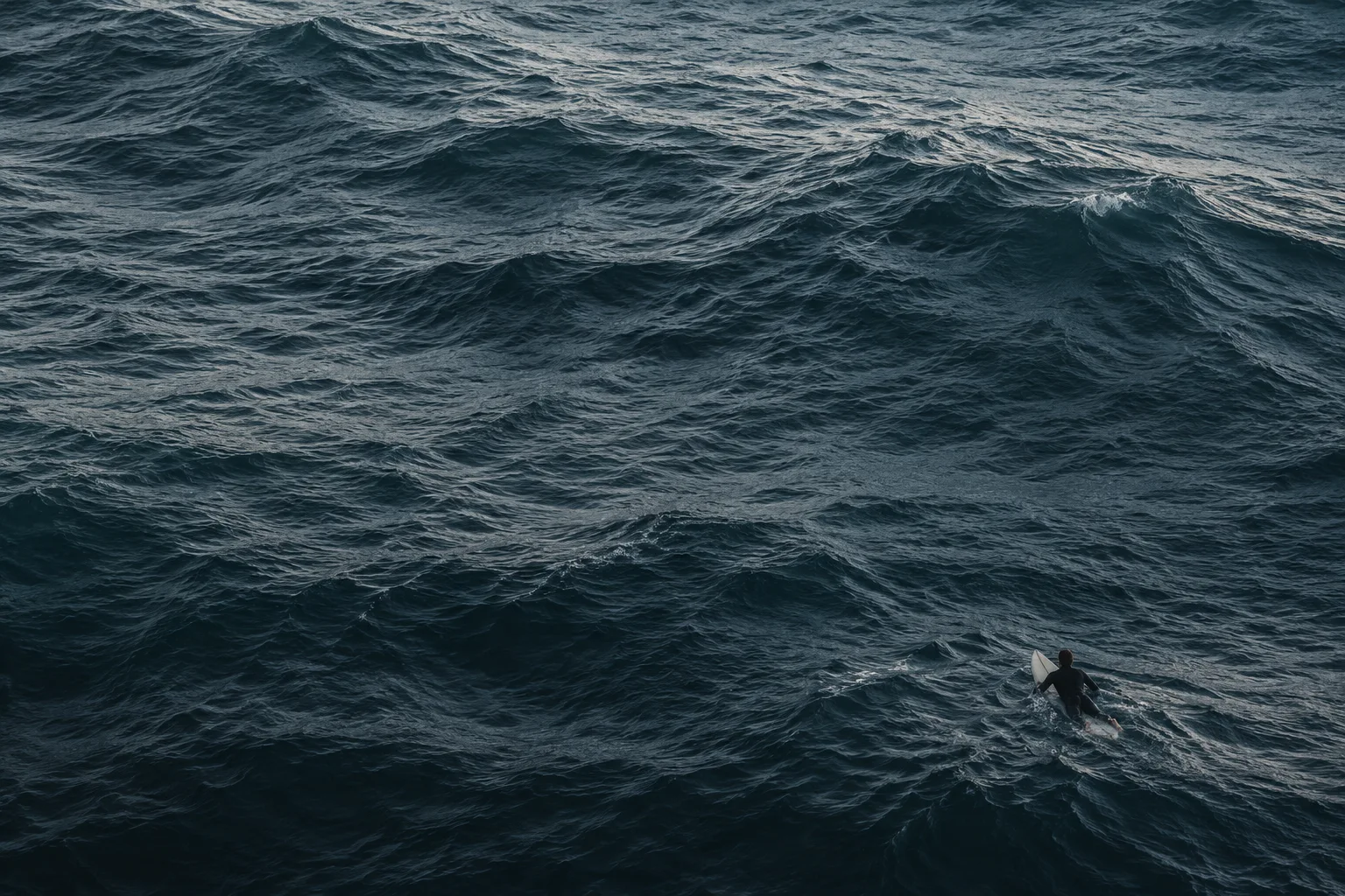 A small surfer floating in a vast, textured blue ocean